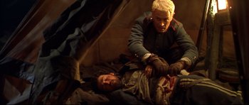 Movie still from “Ravenous” (1999), directed by Antonia Bird – Two men are laying on the ground and one is lying on the ground; Medium shot, High angle