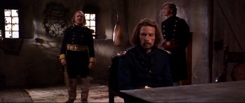 Movie still from “Ravenous” (1999), directed by Antonia Bird – A man in a military uniform sitting in front of two other men; Medium shot, Over the shoulder angle