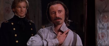 Movie still from “Ravenous” (1999), directed by Antonia Bird – A man with long hair and a mustache is wearing a shirt and tie; Close Up shot, Over the shoulder angle
