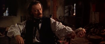 Movie still from “Ravenous” (1999), directed by Antonia Bird – A man with a beard and a mustache is holding a knife; Medium shot, Over the shoulder angle