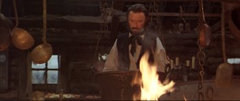 Movie still from “Ravenous” (1999), directed by Antonia Bird – A man standing in front of a fire in a barn; Medium shot, Low angle