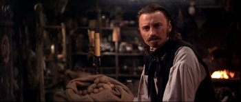 Movie still from “Ravenous” (1999), directed by Antonia Bird – A man with a long hair and a beard standing in front of a bag of potatoes; Close Up shot, Over the shoulder angle