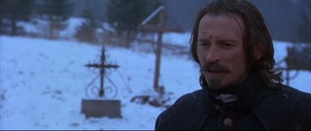 Movie still from “Ravenous” (1999), directed by Antonia Bird – A man standing in front of a cross in the snow; Close Up shot, Over the shoulder angle
