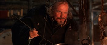 Movie still from “Ravenous” (1999), directed by Antonia Bird – An older man with a beard is holding a pan; Close Up shot, Low angle