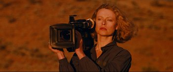 Movie still from “Razorback” (1984), directed by Russell Mulcahy – A woman is holding a video camera up to her face; Close Up shot, Low angle