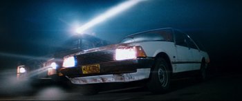 Movie still from “Razorback” (1984), directed by Russell Mulcahy – A car that is parked on the side of the road; Wide shot, Low angle