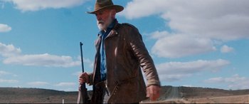 Movie still from “Razorback” (1984), directed by Russell Mulcahy – An old man with a beard wearing a brown jacket and a hat; Medium shot, Low angle
