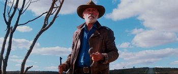 Movie still from “Razorback” (1984), directed by Russell Mulcahy – An older man wearing a cowboy hat holding a wrench; Medium shot, Low angle