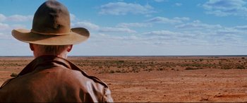 Movie still from “Razorback” (1984), directed by Russell Mulcahy – A man standing in the middle of an open field; Wide shot, Over the shoulder angle