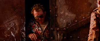 Movie still from “Razorback” (1984), directed by Russell Mulcahy – A man in a floral shirt leaning against a metal wall; Close Up shot, Low angle
