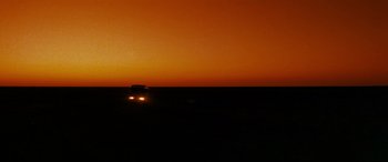 Movie still from “Razorback” (1984), directed by Russell Mulcahy – A car driving on a road at sunset; Extreme Wide shot, Over the shoulder angle