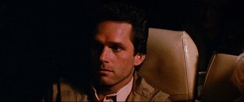 Movie still from “Razorback” (1984), directed by Russell Mulcahy – A person sitting in a chair wearing a jacket; Close Up shot, Over the shoulder angle