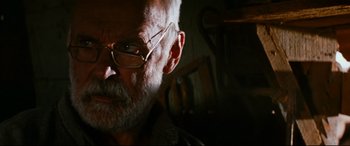 Movie still from “Razorback” (1984), directed by Russell Mulcahy – An older man wearing glasses looking at the camera; Close Up shot, Low angle