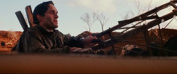 Movie still from “Razorback” (1984), directed by Russell Mulcahy – A man holding on to a gun while standing in a field; Close Up shot, Low angle