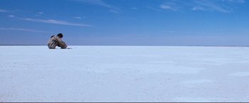 Movie still from “Razorback” (1984), directed by Russell Mulcahy – A large expanse of white sand with a blue sky in the background; Extreme Wide shot, High angle
