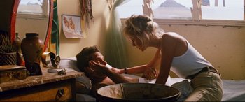 Movie still from “Razorback” (1984), directed by Russell Mulcahy – A man and a woman are in a room together; Medium shot, Over the shoulder angle