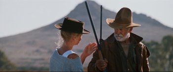 Movie still from “Razorback” (1984), directed by Russell Mulcahy – A man and a woman holding sticks in a field; Medium shot, Over the shoulder angle