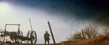 Movie still from “Razorback” (1984), directed by Russell Mulcahy – A man standing next to a pole with a gun in front of it; Wide shot, Low angle