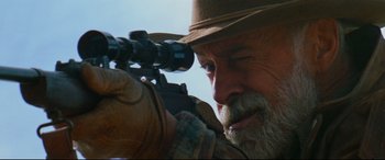 Movie still from “Razorback” (1984), directed by Russell Mulcahy – An old man with a beard and a hat is looking through a scope; Close Up shot, Over the shoulder angle
