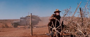 Movie still from “Razorback” (1984), directed by Russell Mulcahy – An old man sitting next to an old wagon wheel; Wide shot, Low angle