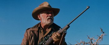 Movie still from “Razorback” (1984), directed by Russell Mulcahy – An older man holding a rifle in his hand; Medium shot, Low angle