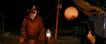 Movie still from “Razorback” (1984), directed by Russell Mulcahy – An old man in a hat and a hat stands next to a lantern; Wide shot, Over the shoulder angle