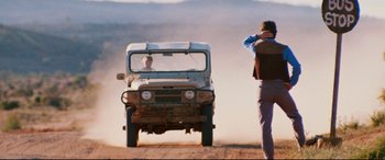 Movie still from “Razorback” (1984), directed by Russell Mulcahy – A man standing in front of an off road vehicle on a dirt road; Wide shot, Over the shoulder angle