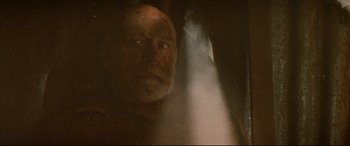 Movie still from “Razorback” (1984), directed by Russell Mulcahy – An old man is looking at the camera through a window; Close Up shot, Low angle