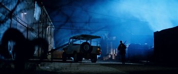 Movie still from “Razorback” (1984), directed by Russell Mulcahy – A man standing next to an old jeep at night; Extreme Wide shot, Low angle