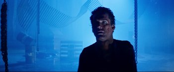 Movie still from “Razorback” (1984), directed by Russell Mulcahy – A man in a black shirt is in a blue room; Close Up shot, Low angle