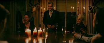 Movie still from “Ready or Not” (2019), directed by Matt Bettinelli-Olpin – A man standing in front of a table with lit candles; Medium shot, Over the shoulder angle