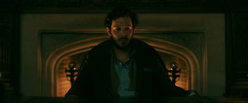 Movie still from “Ready or Not” (2019), directed by Matt Bettinelli-Olpin – A man with a beard is standing in front of a fireplace; Medium shot, Low angle