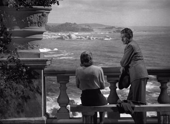 Movie still from “Rebecca” (1940), directed by Alfred Hitchcock – Two women sitting on a bench looking out at the ocean; Wide shot, High angle