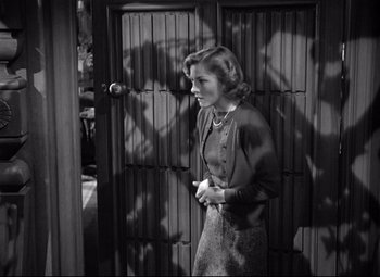 Movie still from “Rebecca” (1940), directed by Alfred Hitchcock – A black - and - white photo of a woman standing in front of a door; Medium shot, High angle