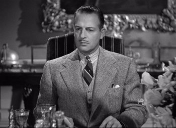 Movie still from “Rebecca” (1940), directed by Alfred Hitchcock – A man in a suit and tie sitting at a table; Close Up shot, Low angle