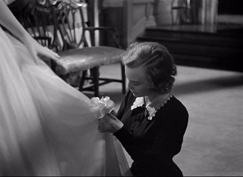 Movie still from “Rebecca” (1940), directed by Alfred Hitchcock – A woman in a black and white photo tying a bow on a dress; Medium shot, Over the shoulder angle