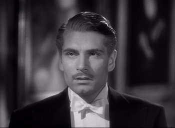 Movie still from “Rebecca” (1940), directed by Alfred Hitchcock – A black and white photo of a man wearing a suit and bow tie; Close Up shot, Over the shoulder angle