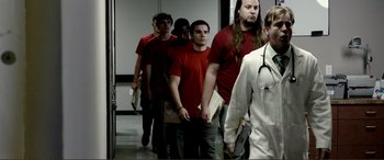 Movie still from “Hostage 911” (2018), directed by Robert Rodriguez – A group of men in red shirts walking down a hall way; Medium shot, Low angle