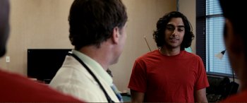 Movie still from “Hostage 911” (2018), directed by Robert Rodriguez – A man in a red t - shirt talking to a doctor; Medium shot, Over the shoulder angle