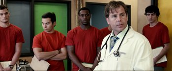 Movie still from “Hostage 911” (2018), directed by Robert Rodriguez – A group of men standing next to each other in front of a doctor; Medium shot, Over the shoulder angle