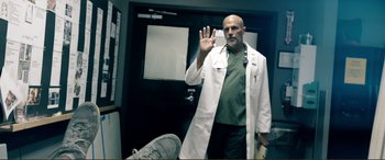 Movie still from “Hostage 911” (2018), directed by Robert Rodriguez – A man in a white lab coat is holding his hand up; Medium shot, Low angle