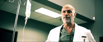 Movie still from “Hostage 911” (2018), directed by Robert Rodriguez – A man with a beard is wearing a lab coat; Medium shot, Low angle