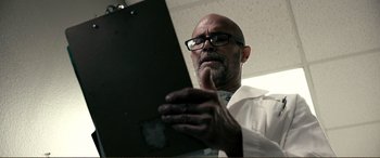 Movie still from “Hostage 911” (2018), directed by Robert Rodriguez – A man in a white lab coat looking at a clipboard; Close Up shot, Low angle