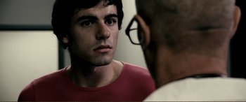 Movie still from “Hostage 911” (2018), directed by Robert Rodriguez – A young man looking into a mirror while wearing a red t - shirt; Close Up shot, Over the shoulder angle