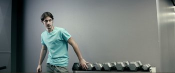 Movie still from “Hostage 911” (2018), directed by Robert Rodriguez – A man standing in front of a row of dumbbells; Medium shot, Low angle