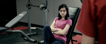 Movie still from “Hostage 911” (2018), directed by Robert Rodriguez – A woman sitting in a chair with her arms crossed in a gym; Medium shot, High angle