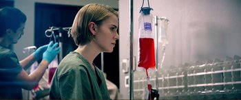 Movie still from “Hostage 911” (2018), directed by Robert Rodriguez – A woman in a green lab coat looking at an empty blood bag; Close Up shot, Low angle
