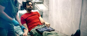 Movie still from “Hostage 911” (2018), directed by Robert Rodriguez – A man sitting on top of a bed holding a keyboard; Medium shot, Overhead angle