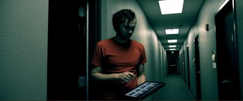 Movie still from “Hostage 911” (2018), directed by Robert Rodriguez – A man in a red t - shirt holding a keyboard; Medium shot, High angle