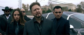 Movie still from “Hostage 911” (2018), directed by Robert Rodriguez – A group of men standing next to each other in a parking lot; Medium shot, Over the shoulder angle